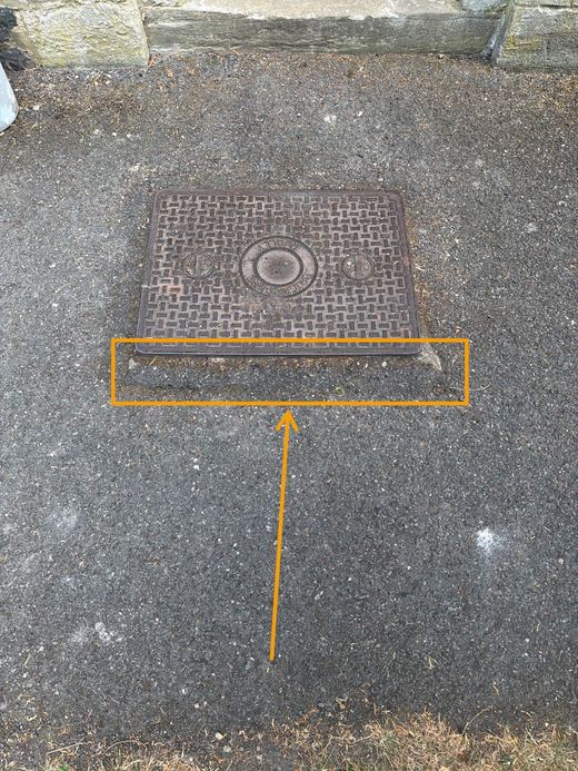 Sunken manhole surround marked up as a trip hazard with an orange box and arrow